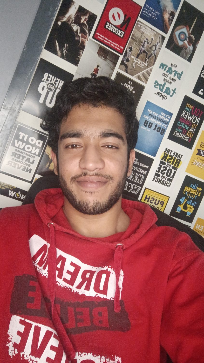 Sumit off duty in a red hoodie, smiling, in his room.