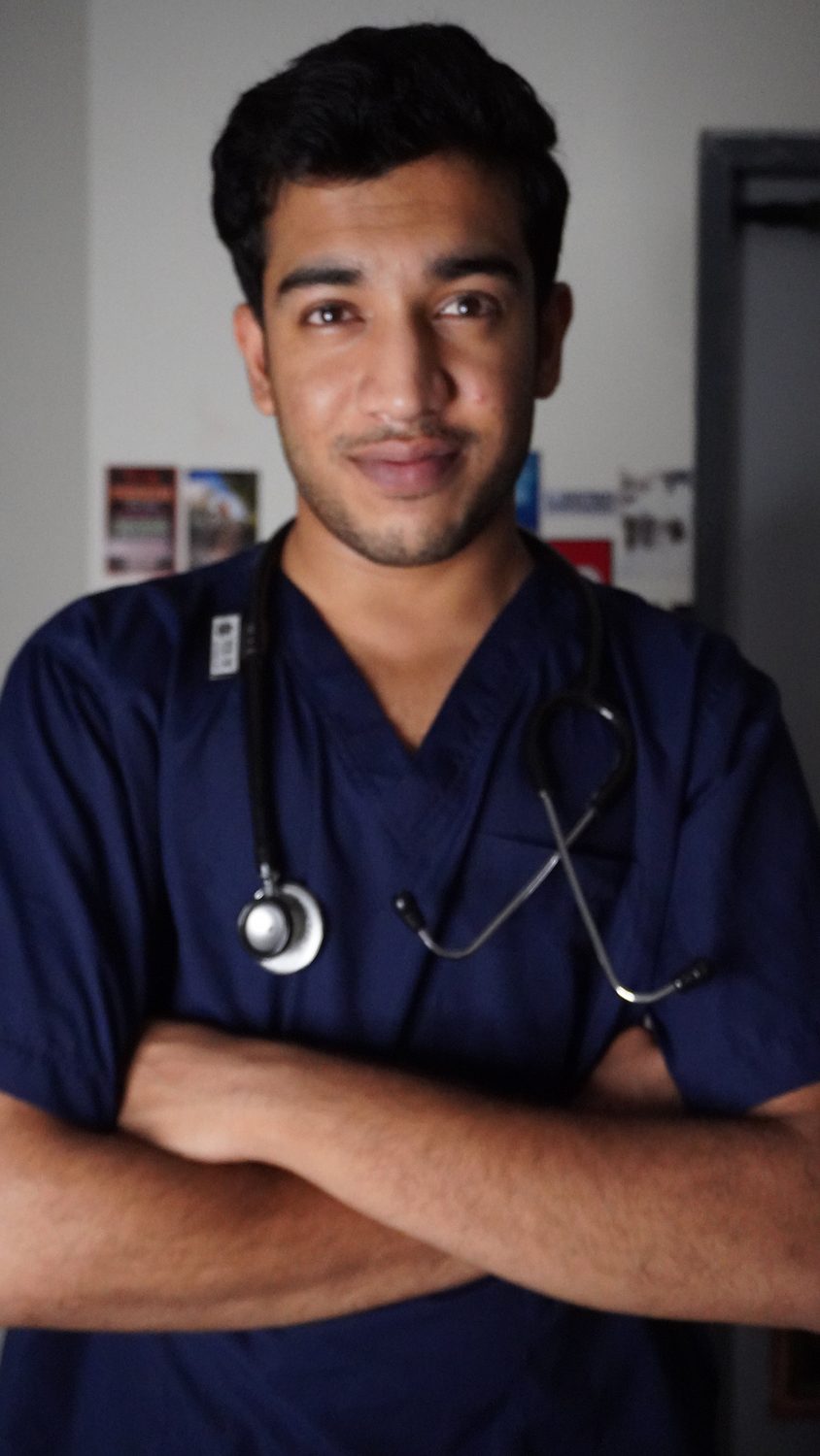 Dr. Sumit Wanjari in navy scrubs with a stethoscope, arms crossed, on shift.