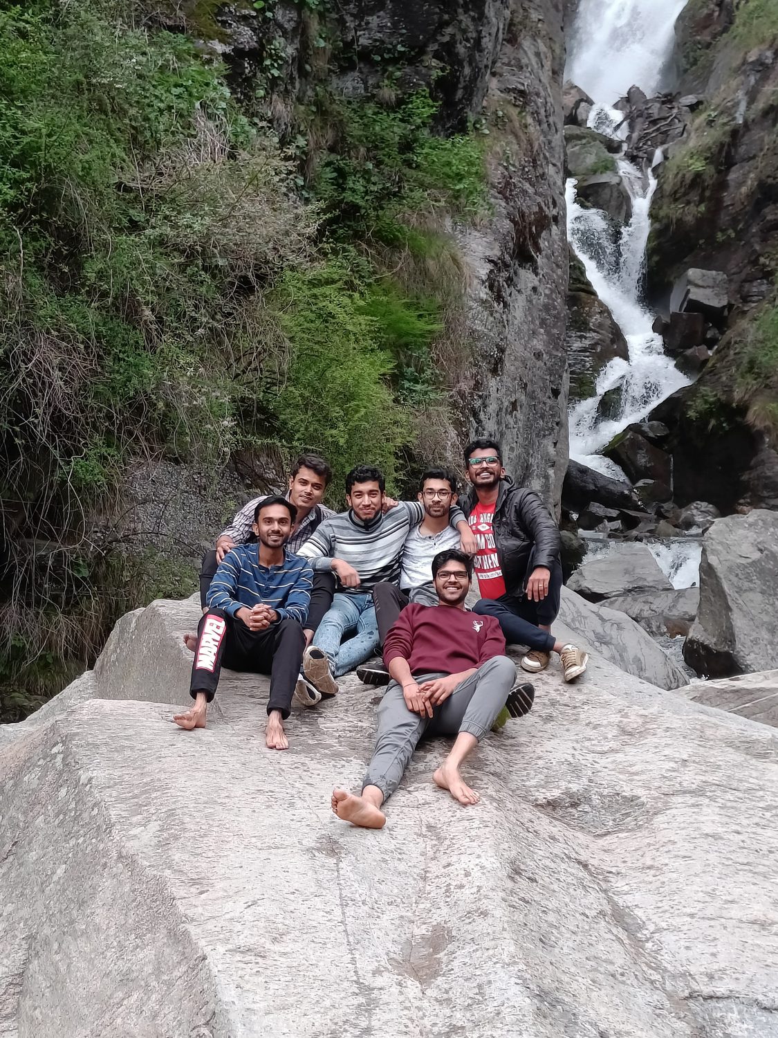 Sumit and friends resting on rocks by a waterfall.