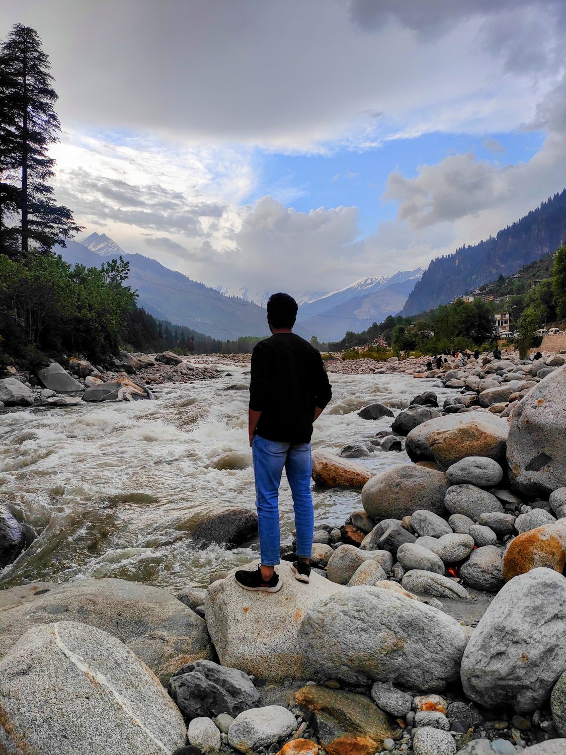 Sumit standing on river rocks with mountains behind.