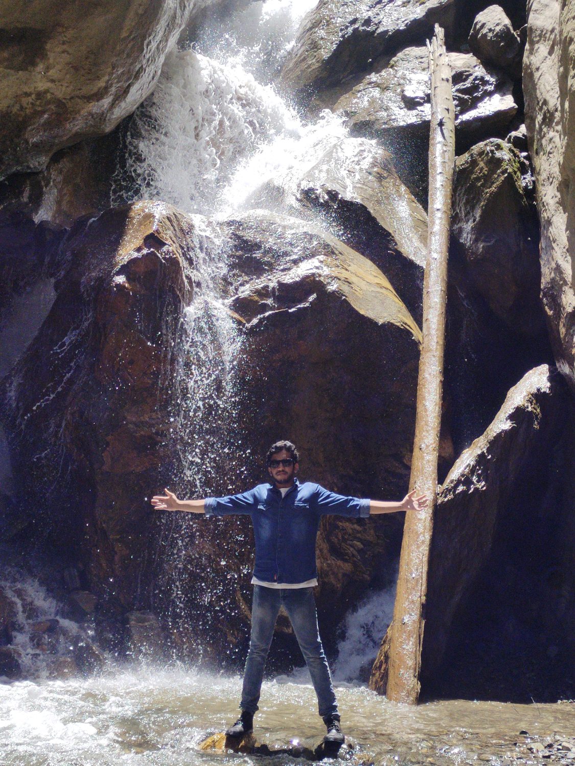 Sumit standing with arms spread in front of a waterfall.